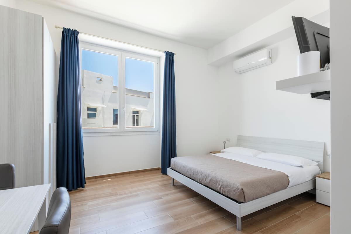 A modern hotel room with a bed, a desk, and a window with curtains.