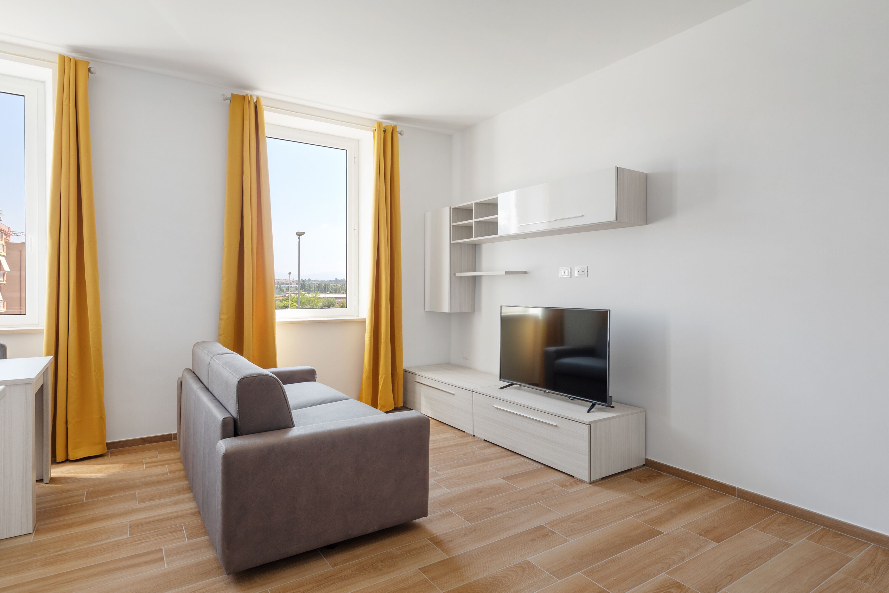 Una sala de estar moderna con sofá, televisor y muebles blancos.