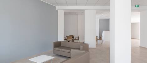 A modern, minimalist lobby with a beige sofa, a small white table, and a dining area in the background.
