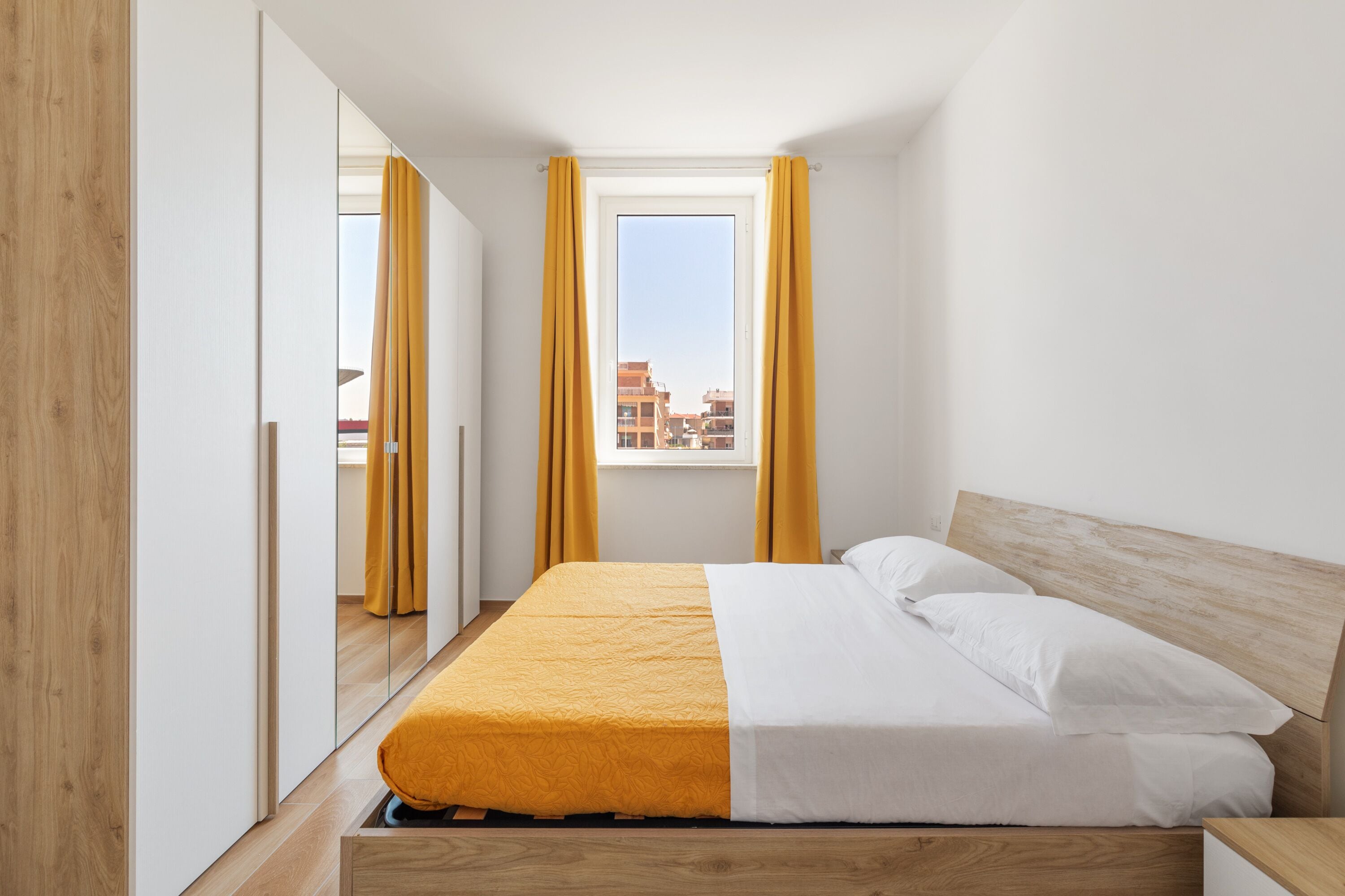 Une chambre à coucher avec un lit, une tête de lit en bois et une fenêtre ornée de rideaux jaunes.