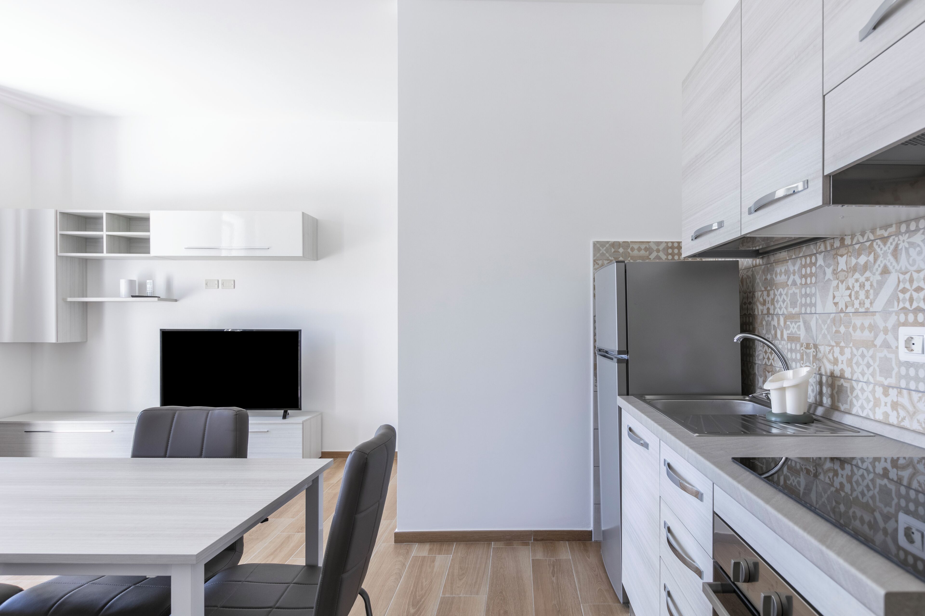 A modern kitchen with white cabinets, a built-in oven, and a large window.