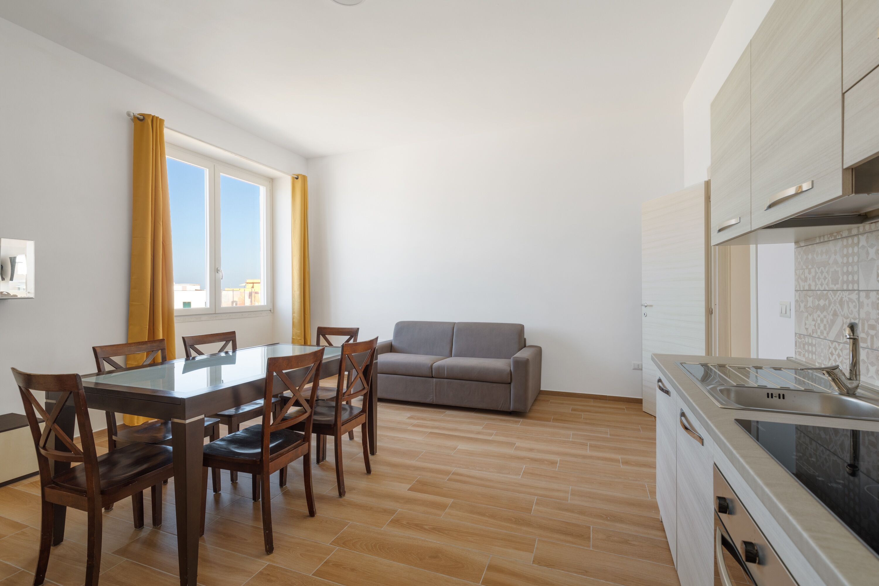 Una cocina moderna con comedor, un sofá gris y una ventana con cortinas amarillas.