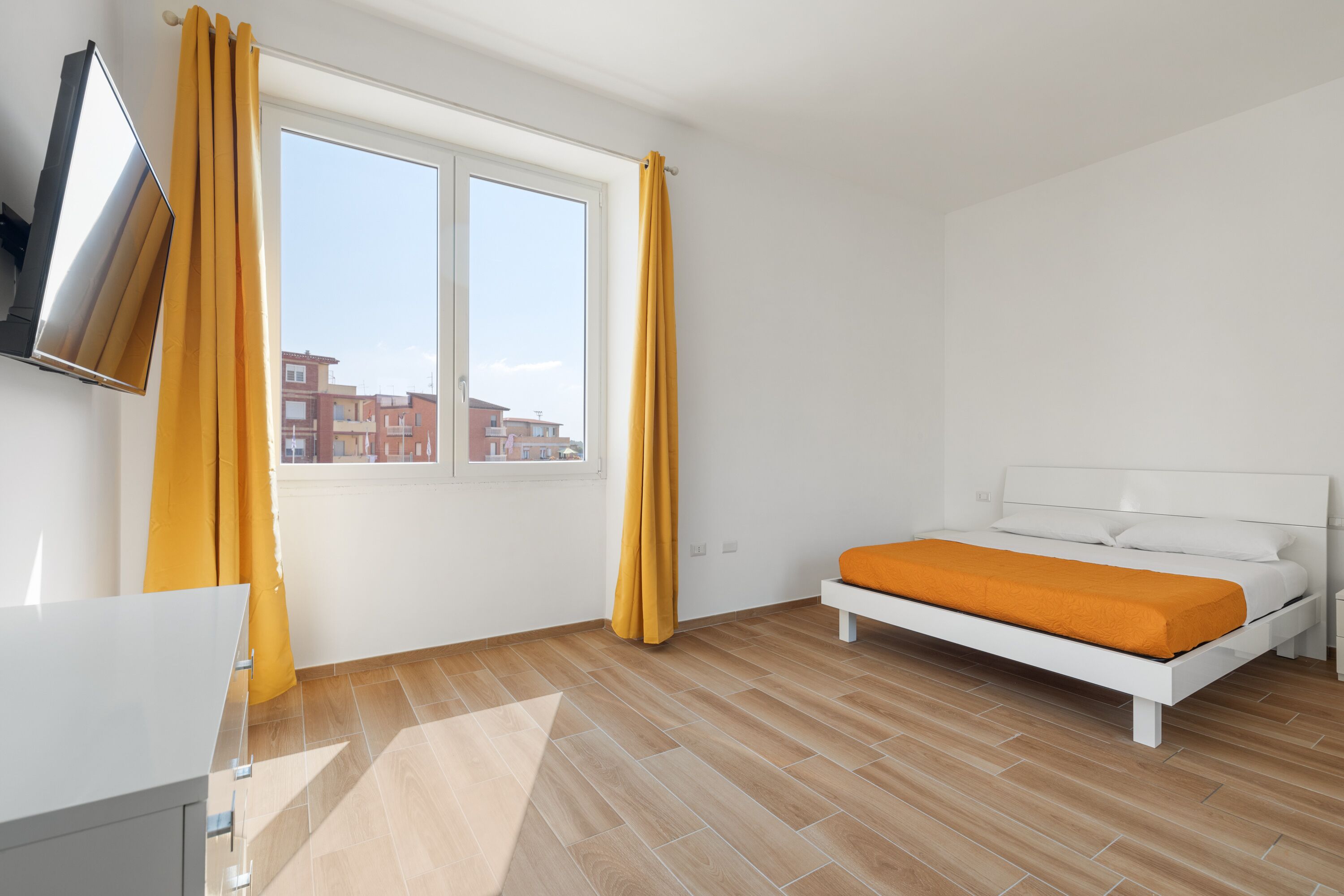 Une chambre à coucher avec un lit, un téléviseur fixé au mur et une fenêtre avec des rideaux.