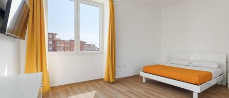 Een slaapkamer met een bed, een aan de muur bevestigde televisie en een raam met gordijnen.