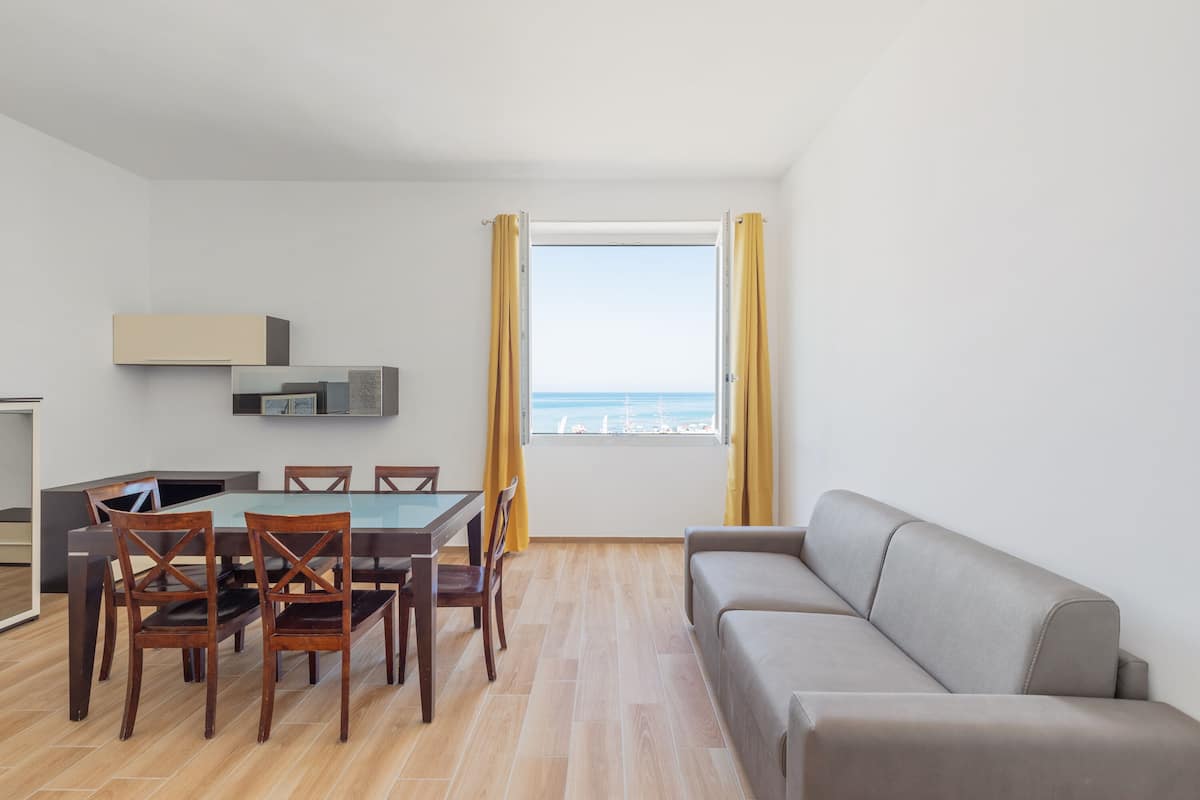A modern living room with a dining area, a sofa, and a view of the sea.