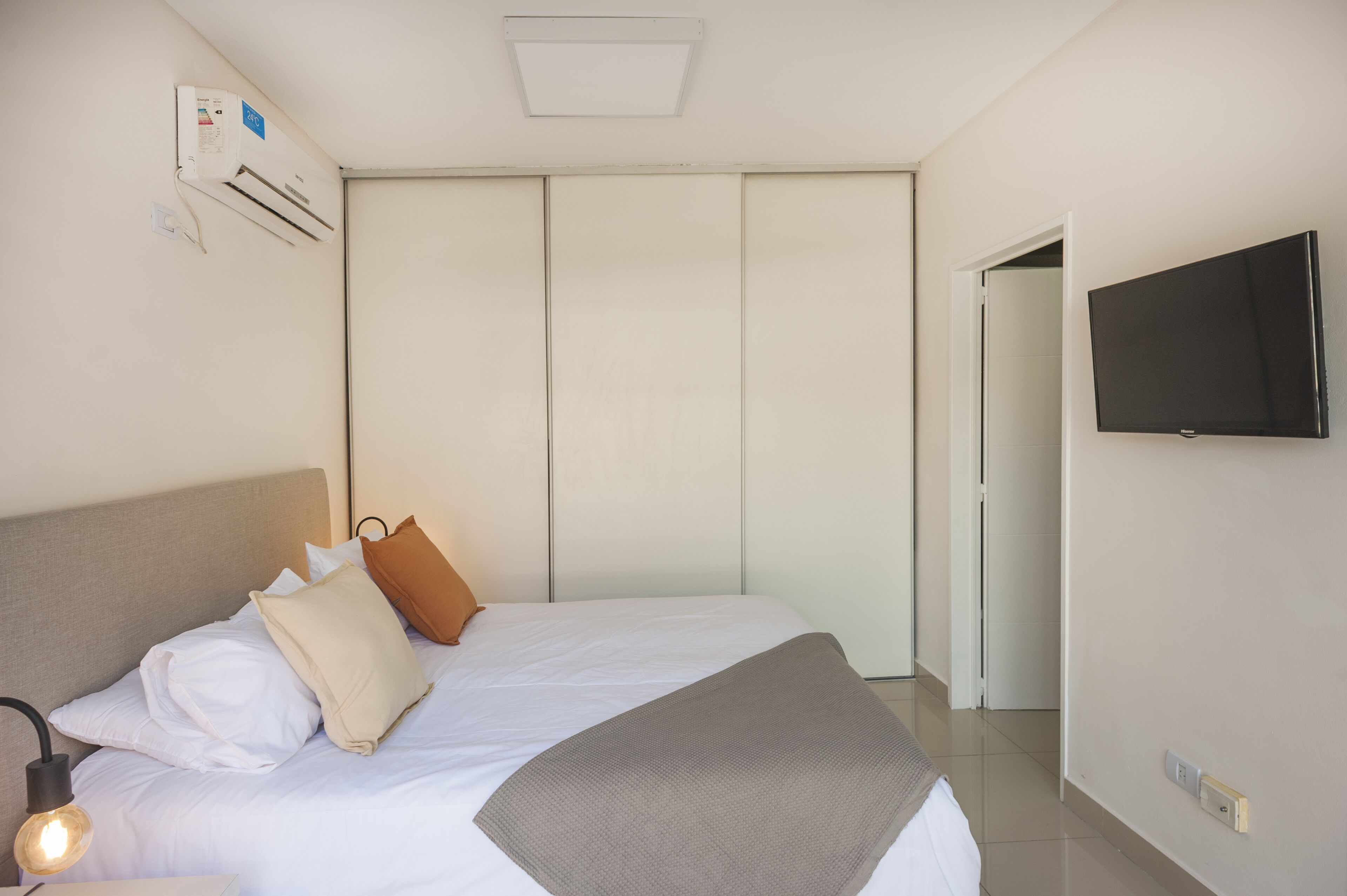 Una habitación de hotel con cama, televisión, aire acondicionado y una puerta.