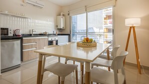 Una cocina moderna con comedor, que cuenta con un amplio ventanal, una lámpara de pie y una cesta de fruta sobre la mesa.