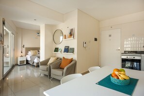 A modern hotel room with a bed, bedside table, chair, and a dining area with a table and fruit bowl. - Báltico Suites  (Buenos Aires)