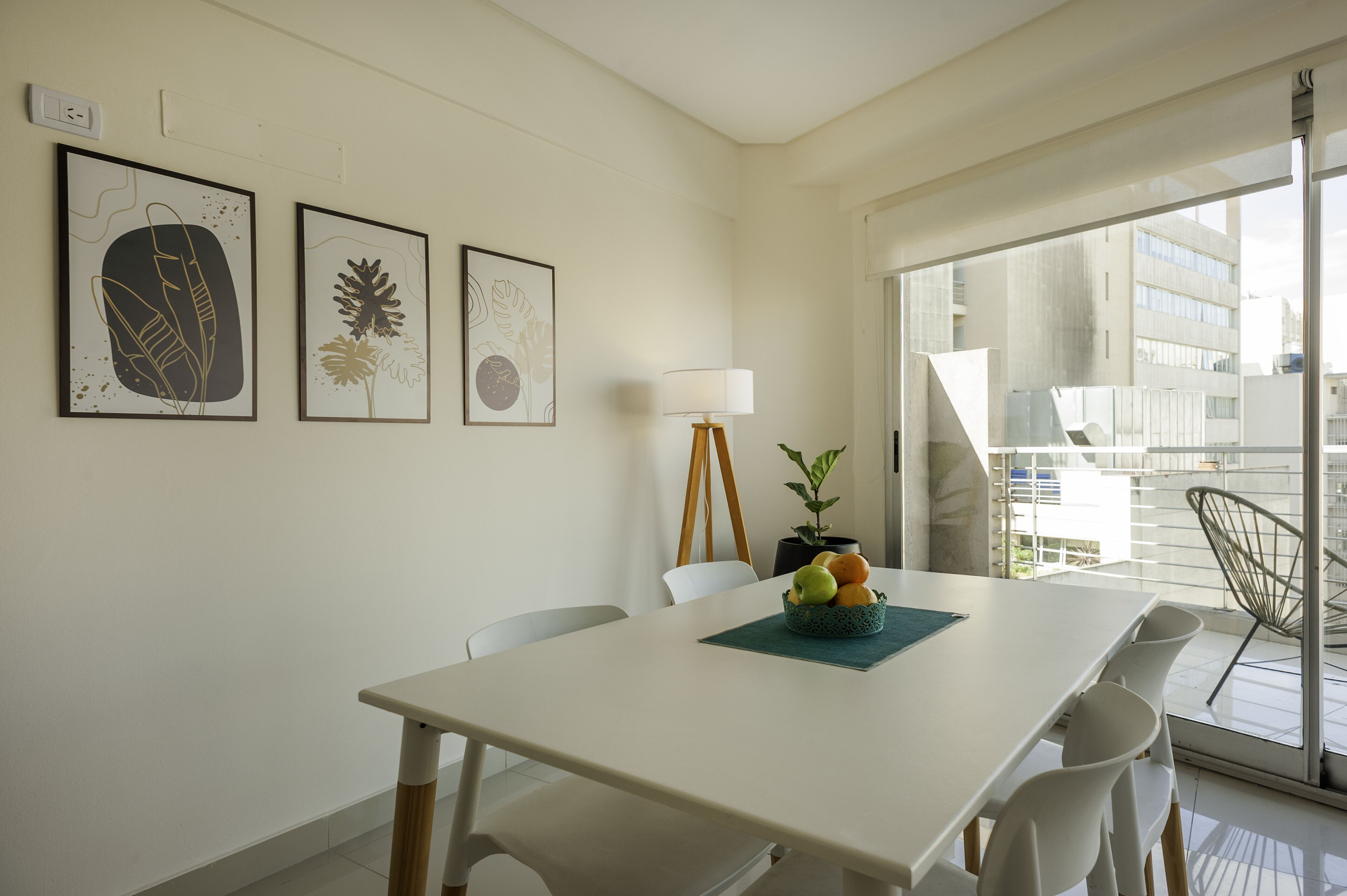 A dining area with a white table, white chairs, a potted plant, and framed artwork on the wall.