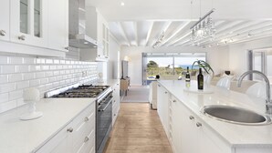 A modern kitchen with white cabinetry, a large island with a sink, and a view to the outdoors. - Sand Plover 85 (Grotto Bay)