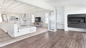 A spacious living area with a white sofa, wooden flooring, a TV, and a sliding glass door. - Sand Plover 85 (Grotto Bay)