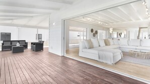 A spacious living area with a large white sofa, a coffee table, and a TV. There is a wooden deck outside the room. - Sand Plover 85 (Grotto Bay)