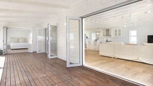 A spacious, modern interior with a wooden deck, a large sliding glass door leading to a living area, and a visible kitchen in the background. - Sand Plover 85 (Grotto Bay)