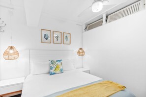 A bedroom with a white bed, a yellow throw blanket, and three framed botanical prints on the wall. - Clifton Studio 104 (Cape Town)
