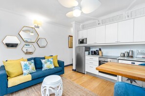 A modern living room with a blue sofa, yellow cushions, and a wooden dining table. - Clifton Studio 104 (Cape Town)