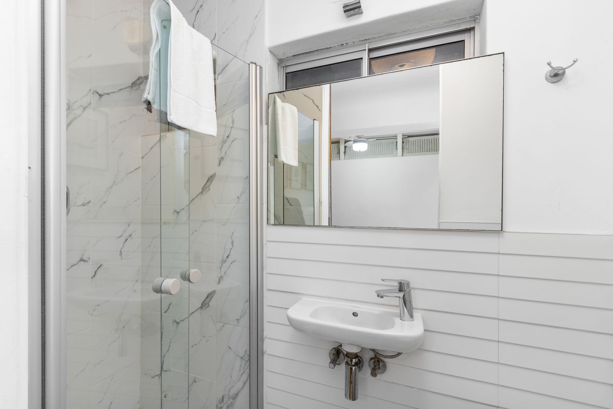 A bathroom with a glass shower enclosure, a white sink, and a mirror above it.