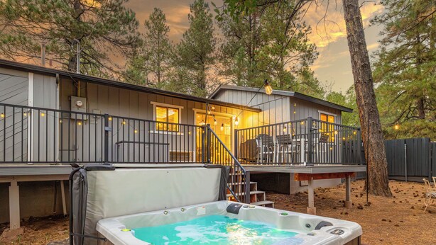 A hot tub in front of a cabin with a deck and stairs leading to the entrance. - Outdoor Oasis: HotTub, Fenced, Firepit & PineTrees (Flagstaff)