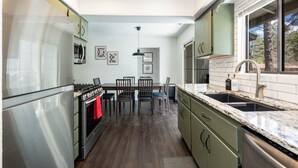 A modern kitchen with a dining area, stainless steel appliances, and a large window. - Outdoor Oasis: HotTub, Fenced, Firepit & PineTrees (Flagstaff)