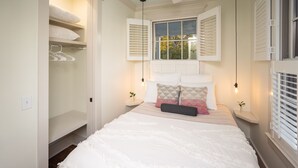 A bedroom with a bed, a closet, and a window with shutters. - The Harrington in downtown Beaufort  (Beaufort)