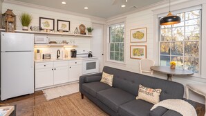 A kitchen with white cabinets, a gray sofa, and a dining table. - The Harrington in downtown Beaufort  (Beaufort)