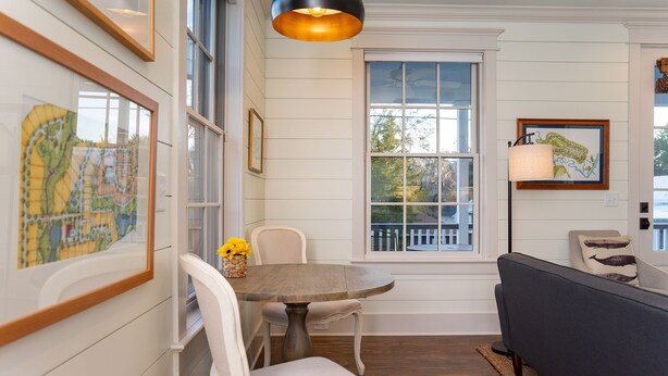 A dining area with a round wooden table, white chairs, and a dark-colored sofa. - The Harrington in downtown Beaufort  (Beaufort)