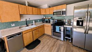 A modern kitchen with wooden cabinets, stainless steel appliances, a dishwasher, and a tiled backsplash. - Emerald Lake House- Boat Parking with a View of the Vermillion Cliffs (Page)