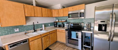 A modern kitchen with wooden cabinets, stainless steel appliances, a dishwasher, and a tiled backsplash.
