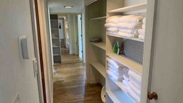 A hallway with wooden flooring leading to a closet with shelves holding folded towels and an ironing board. - Emerald Lake House- Boat Parking with a View of the Vermillion Cliffs (Page)