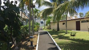 A pathway lined with palm trees and a building with a sign that reads "EXCURSION". - Super Appartement Avec Piscine, en Plein Coeur du Centre Ville de la Marina (Le Gosier)