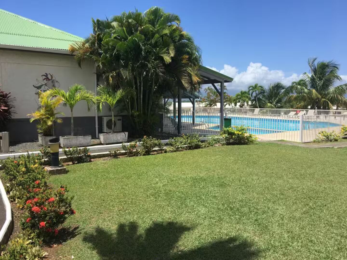 Un espace piscine doté d’un coin salon abrité, de palmiers et d’un bâtiment surmonté d’un toit végétalisé.