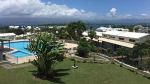 A residential area with a swimming pool, palm trees, and a view of the ocean and mountains. - Super Appartement Avec Piscine, en Plein Coeur du Centre Ville de la Marina (Le Gosier)