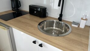 A kitchen with a stainless steel sink, a black toaster, and a black kettle on a wooden countertop. - Super Appartement Avec Piscine, en Plein Coeur du Centre Ville de la Marina (Le Gosier)