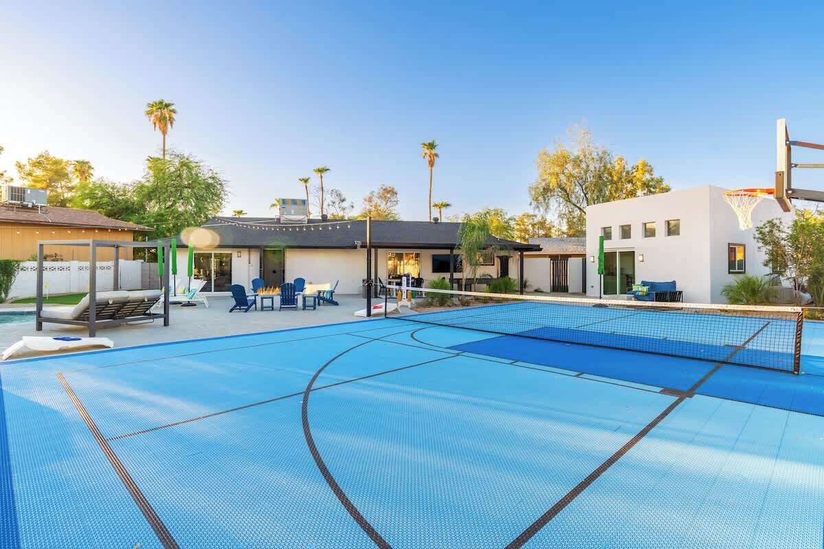 A swimming pool with a basketball court, lounge chairs, and a building with a flat roof.