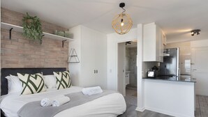 A modern hotel room with a bed, a small kitchen, and a bathroom.