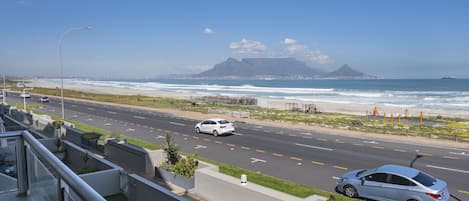 A coastal road with a view of the ocean and a mountain in the distance.