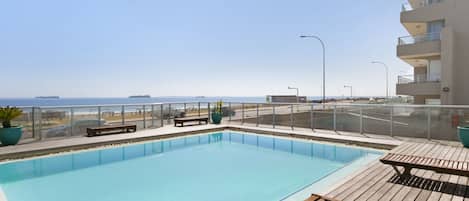A swimming pool with a wooden deck, benches, and potted plants.
