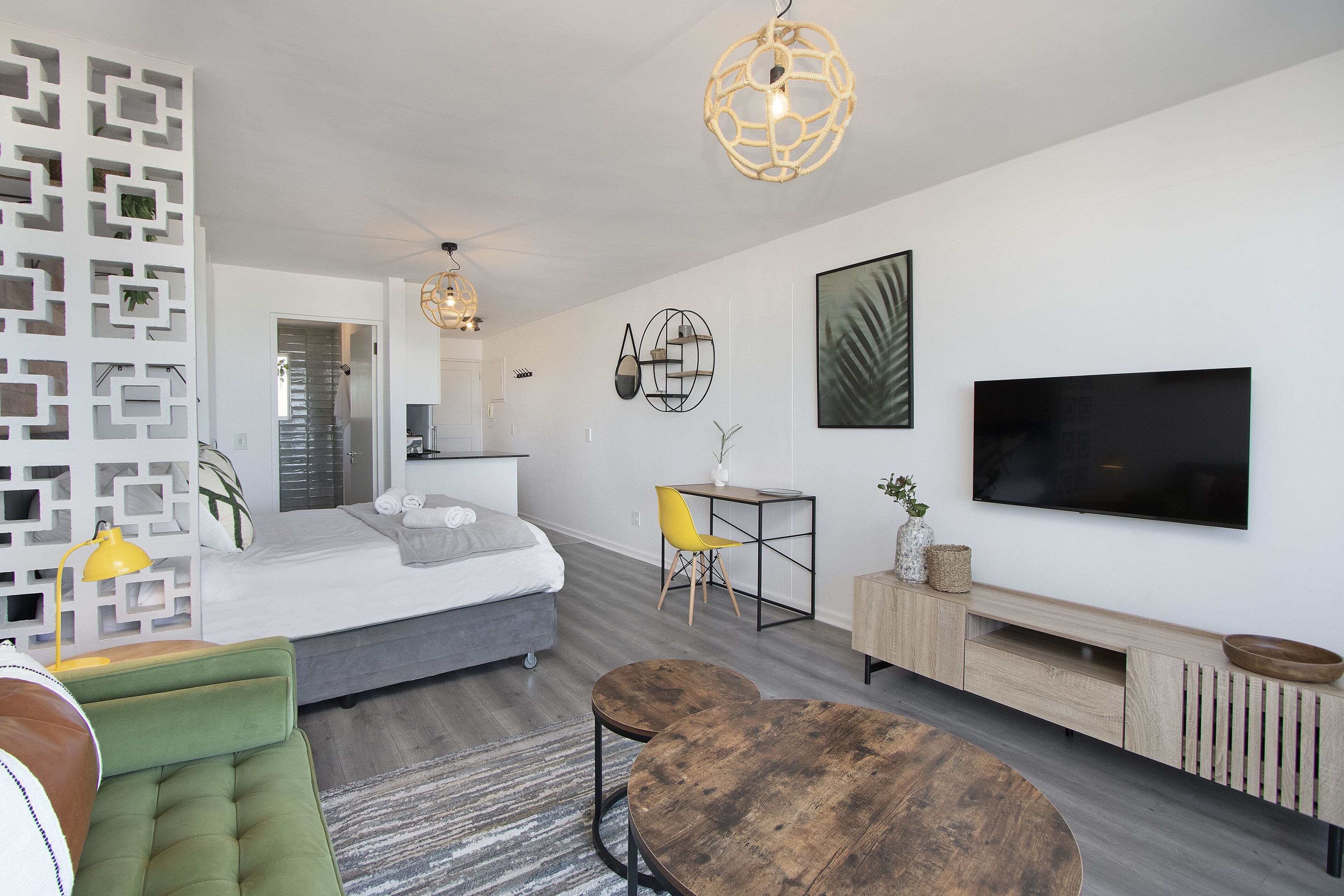 Una sala de estar moderna con una cama, una mesa de comedor, un televisor y una pequeña zona de escritorio.