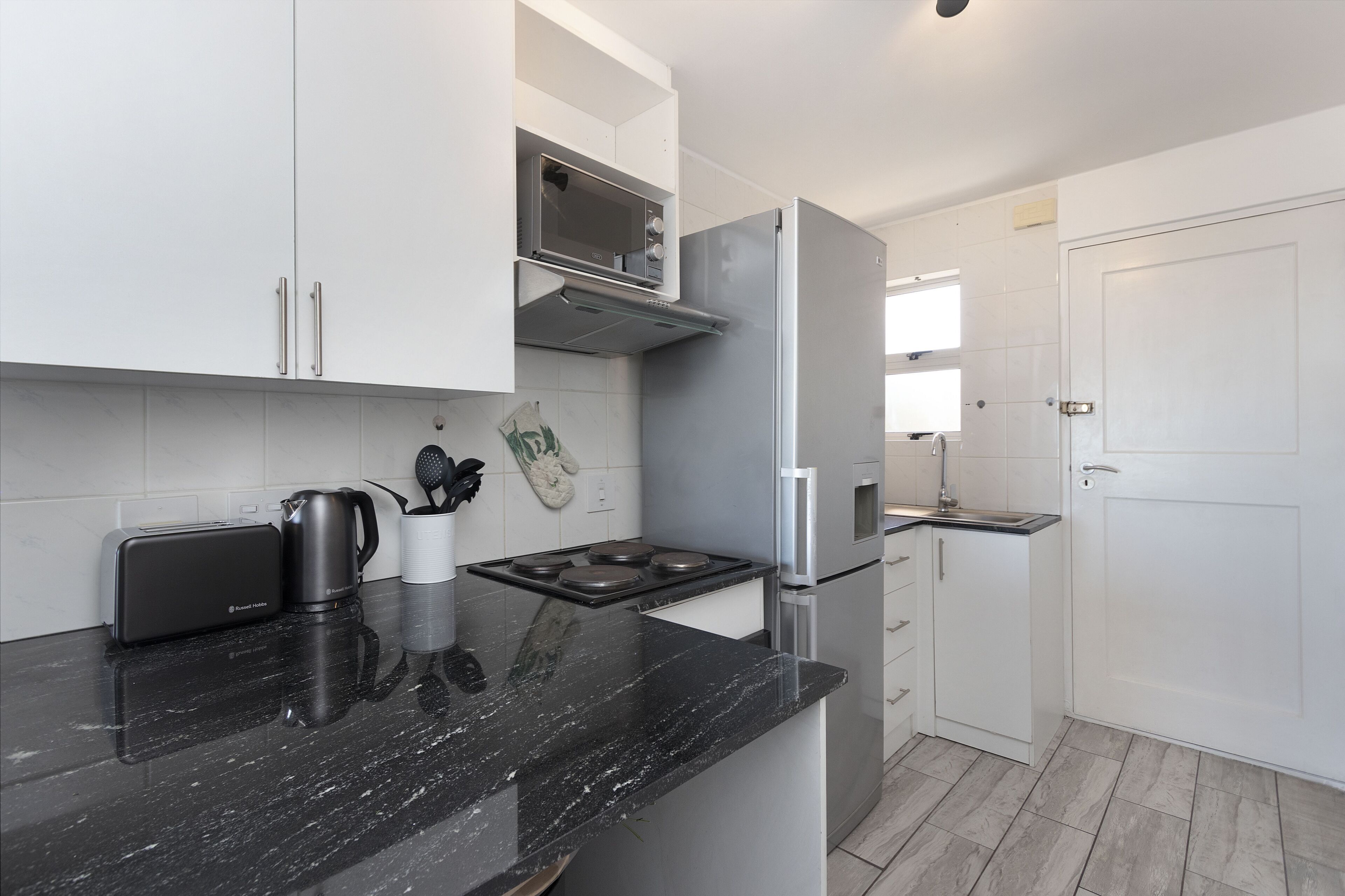 A modern kitchen with white cabinets, a black countertop, a built-in microwave, a stainless steel refrigerator, and a toaster.