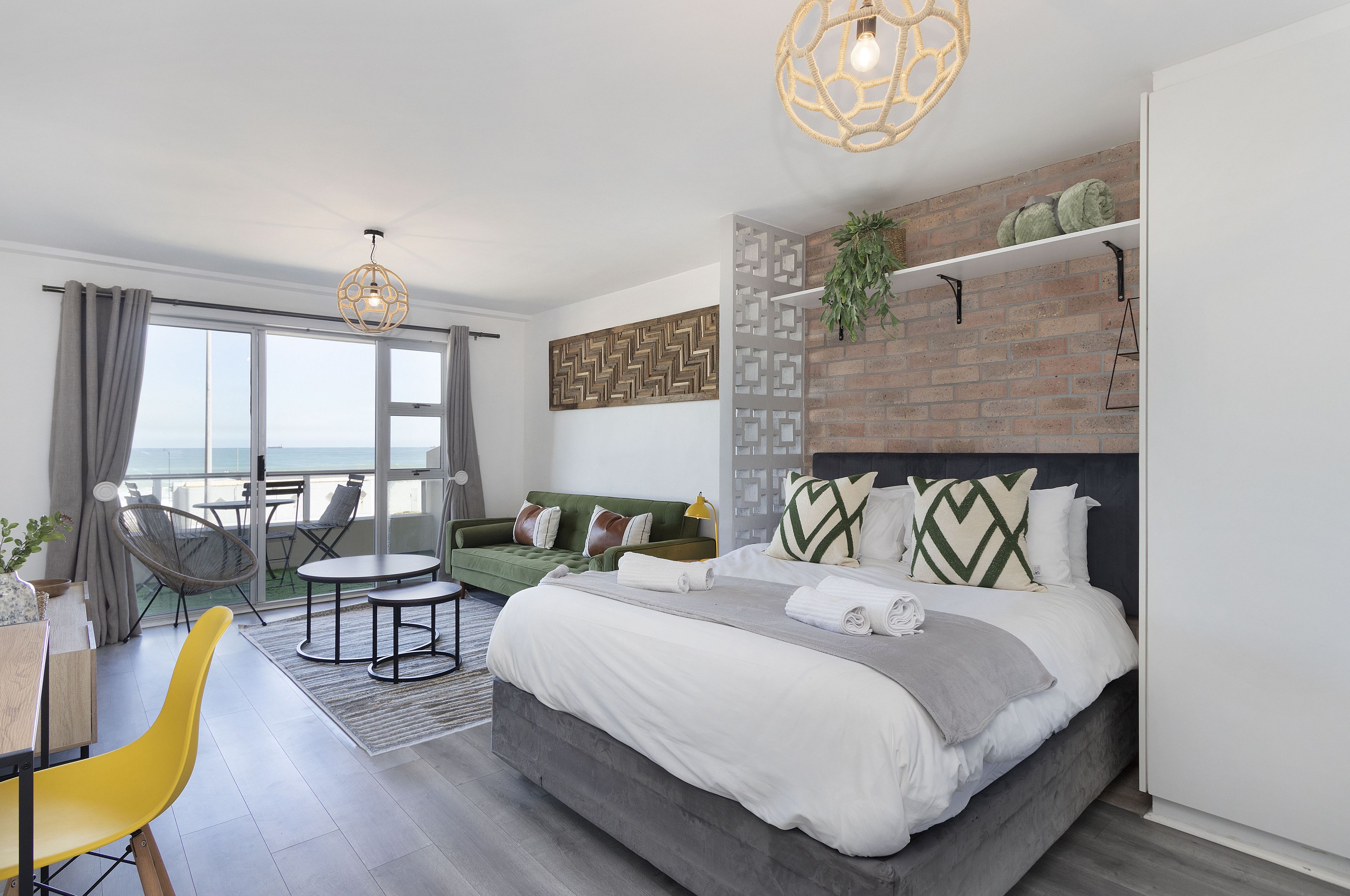 Une chambre d’hôtel moderne dotée d’un grand lit, d’un canapé vert, d’un coin repas et offrant une vue sur la mer.