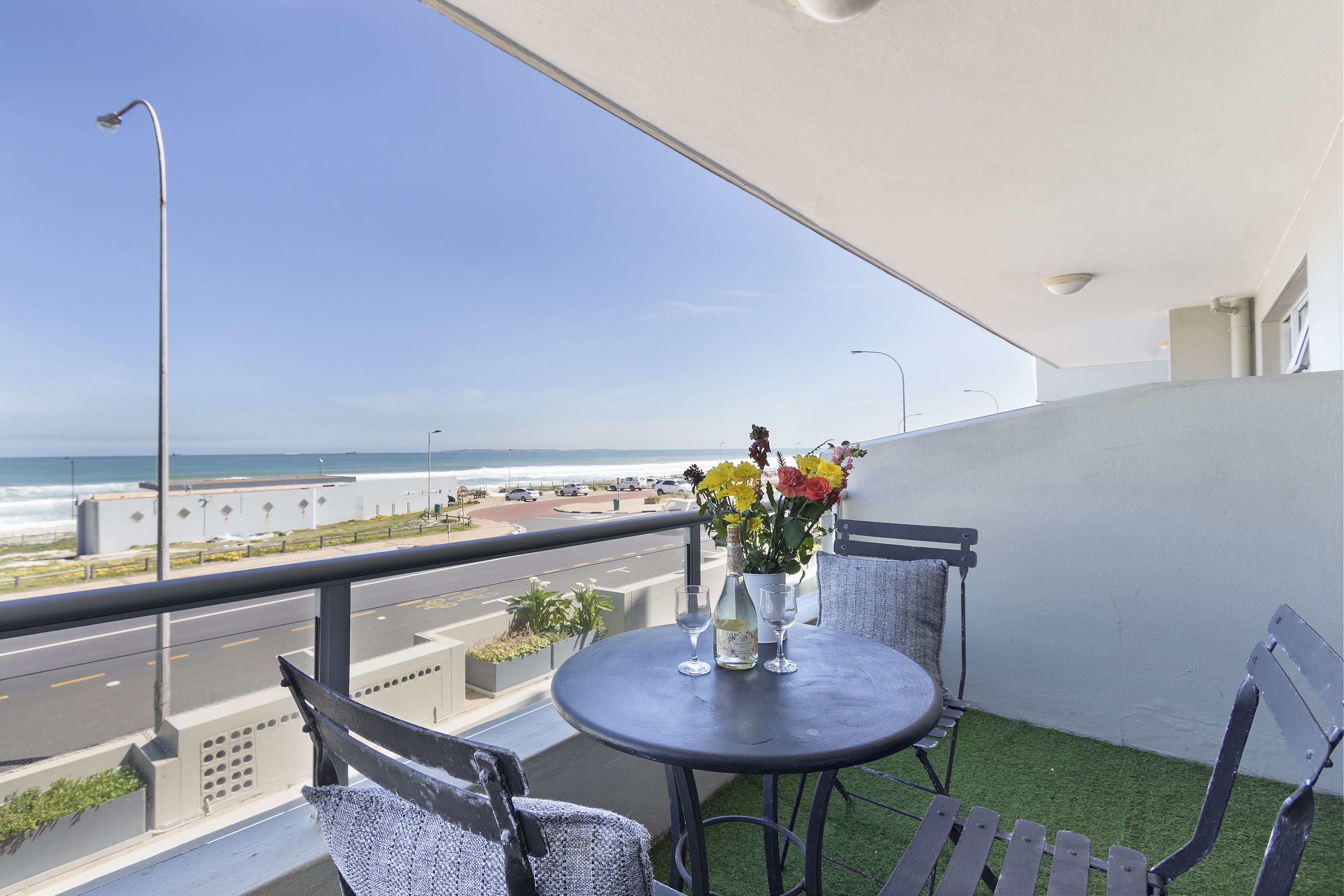 A balcony with a table, chairs, and a vase of flowers.