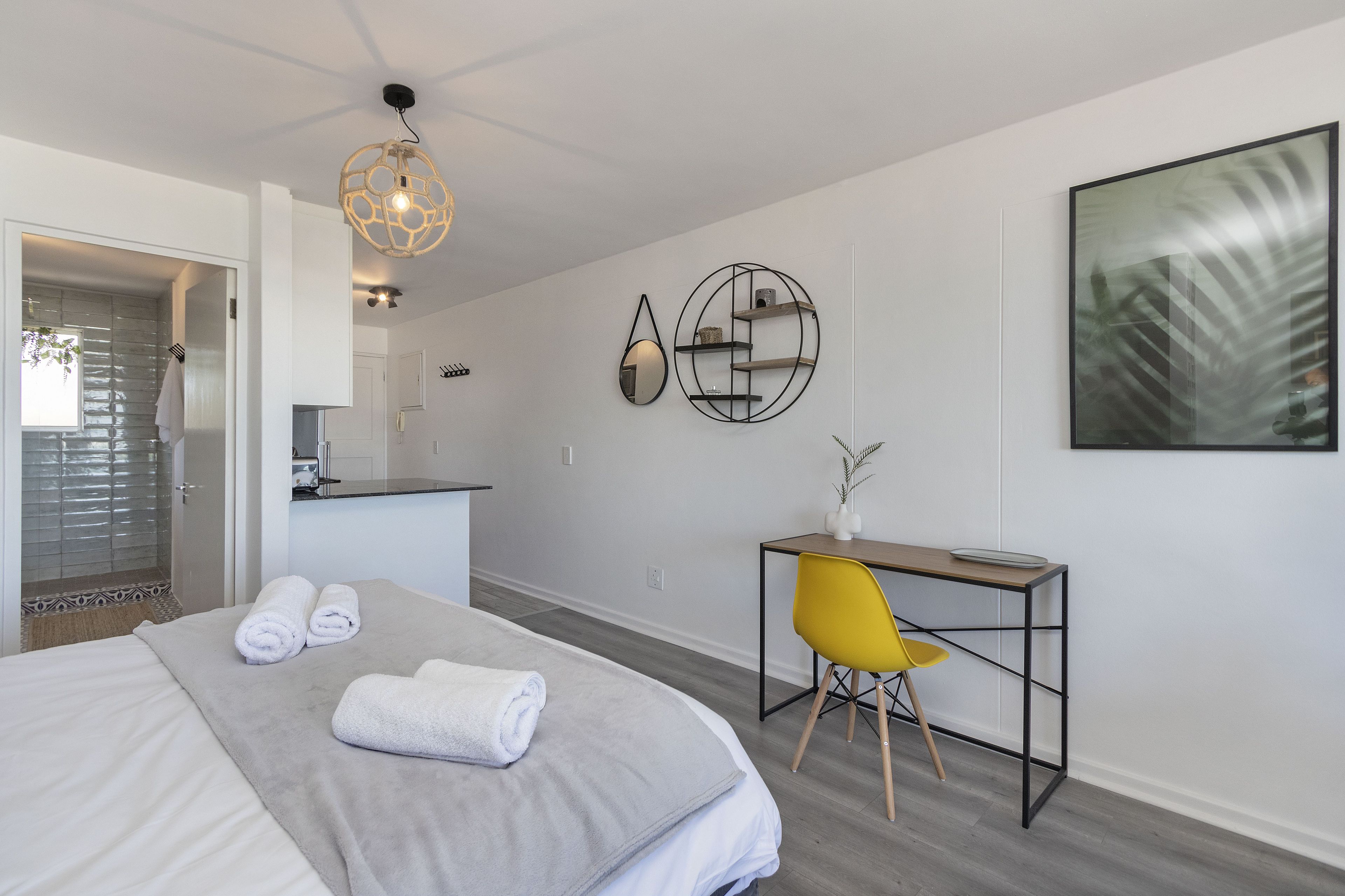 A modern hotel room with a bed, a desk, a chair, and a large window.