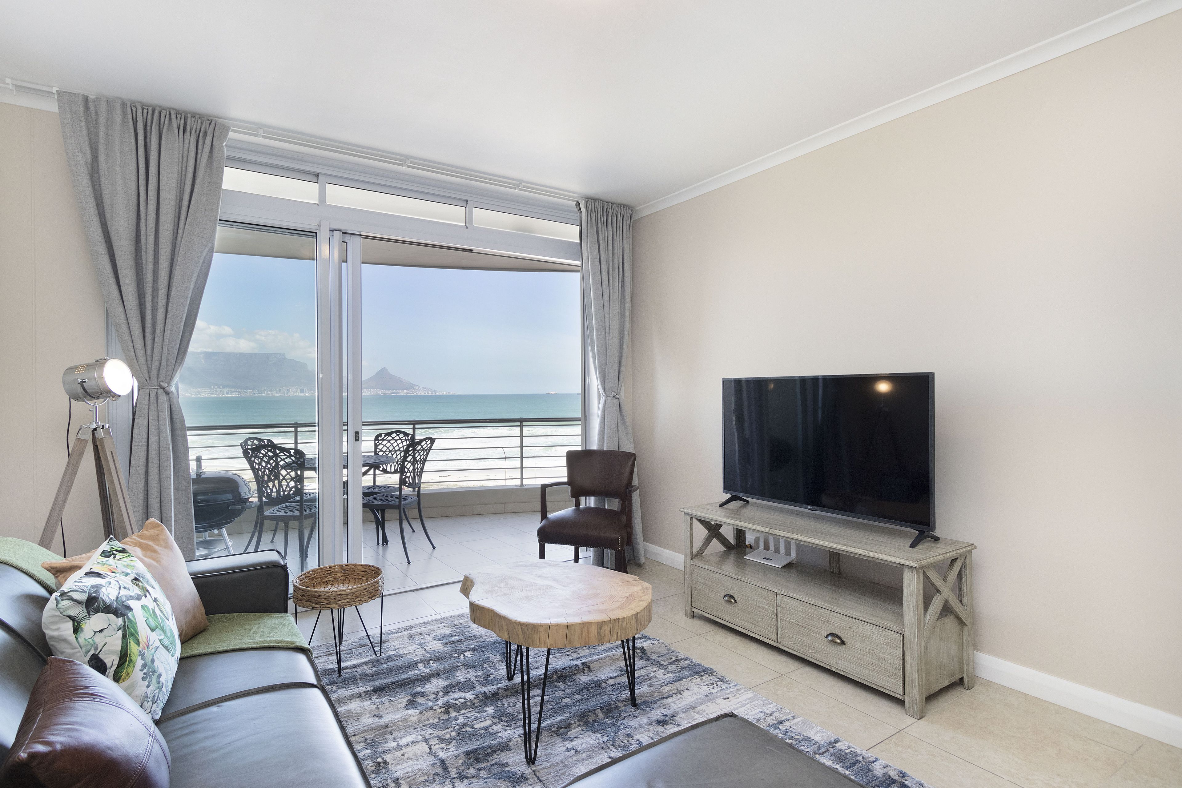 Ein modernes Wohnzimmer mit Sofa, Fernseher, kleinem Tisch und einem Balkon mit Meerblick.