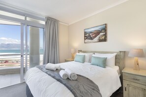 A hotel room with a large bed, a painting on the wall, a view of the ocean, and a balcony with a curtain. - Portico 405 (Cape Town)