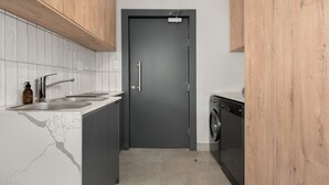 Een kleine keuken met een donkere deur, een wasmachine en een gootsteen met kraan.