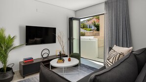 Een moderne woonkamer met een flatscreen televisie, een ronde salontafel, een bank, een klein groen poufje en een plant in pot.
