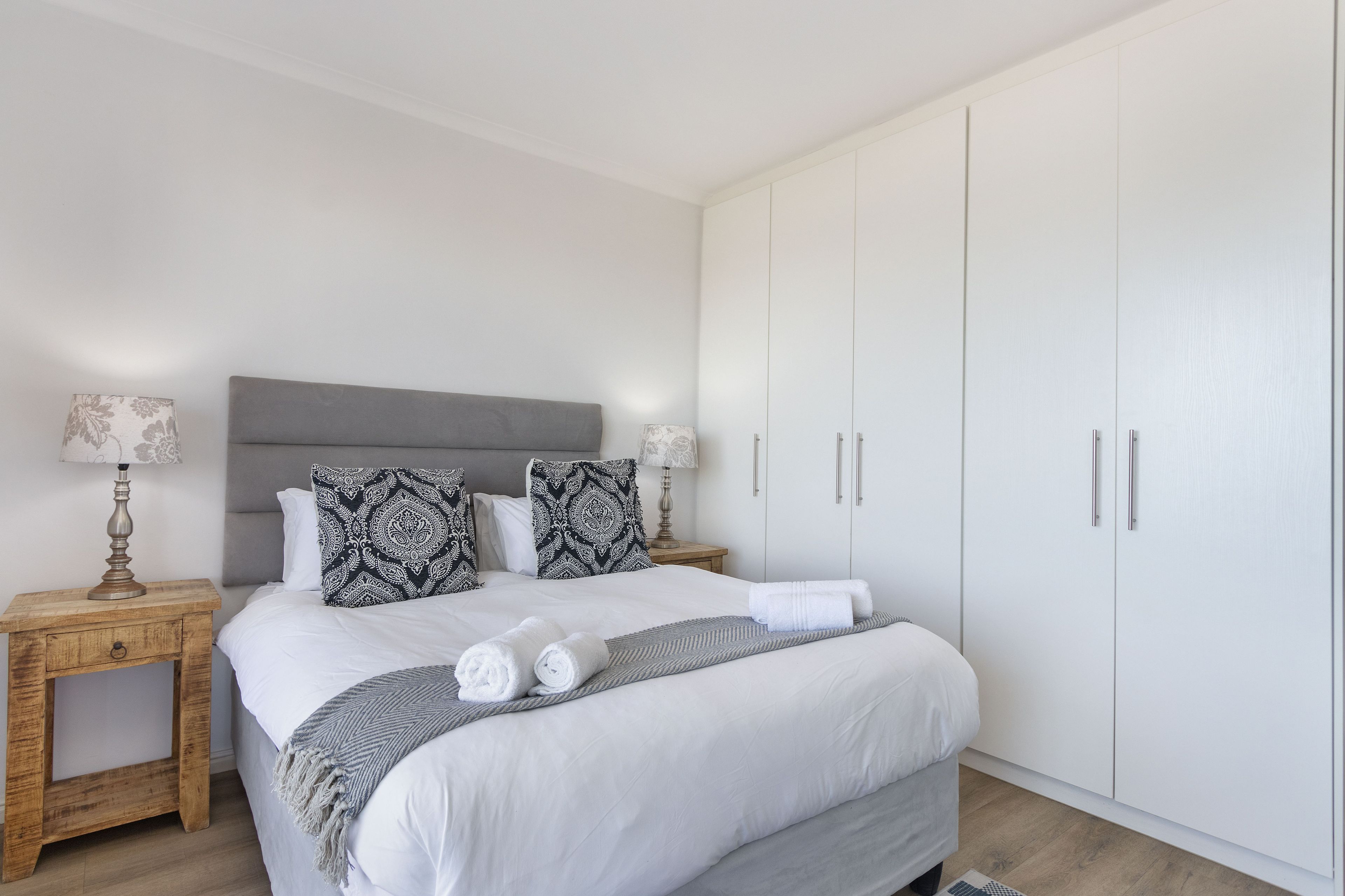 A neatly arranged bedroom with a large bed, two bedside tables with lamps, and a wardrobe.