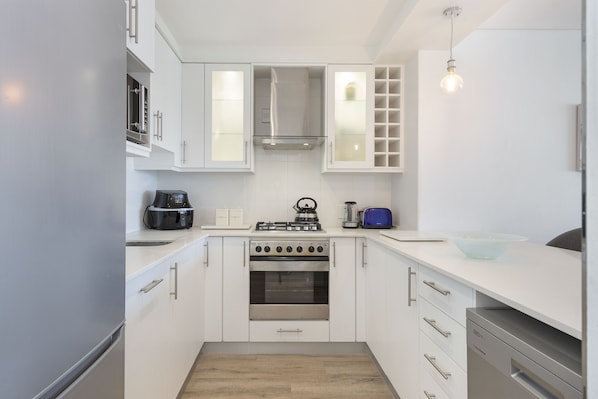 A modern kitchen with white cabinets, a built-in oven, a kettle, and a coffee maker.