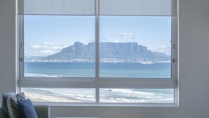 A room with a large window overlooking a beach and mountains.