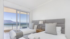 A hotel room with two beds, a view of the ocean, and a balcony.