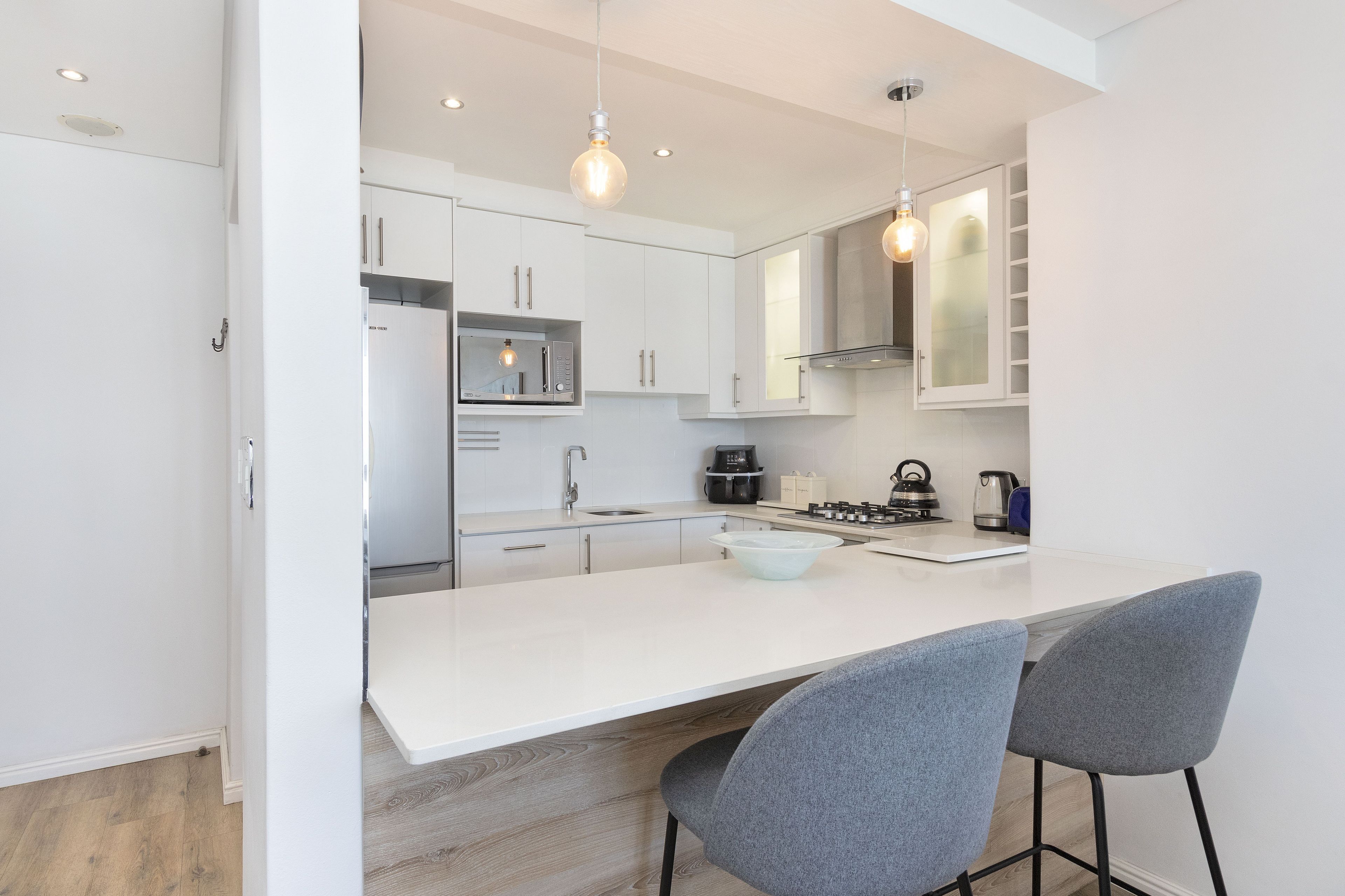 A modern kitchen with white cabinets, a central island with bar stools, and a stainless steel range hood.